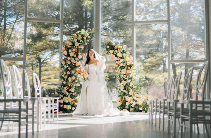 beautiful bride standing in front of floor to ceiling windows next to ceremony arch at summer-inspired wedding