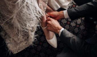 groom helping bride put on shoes on wedding day