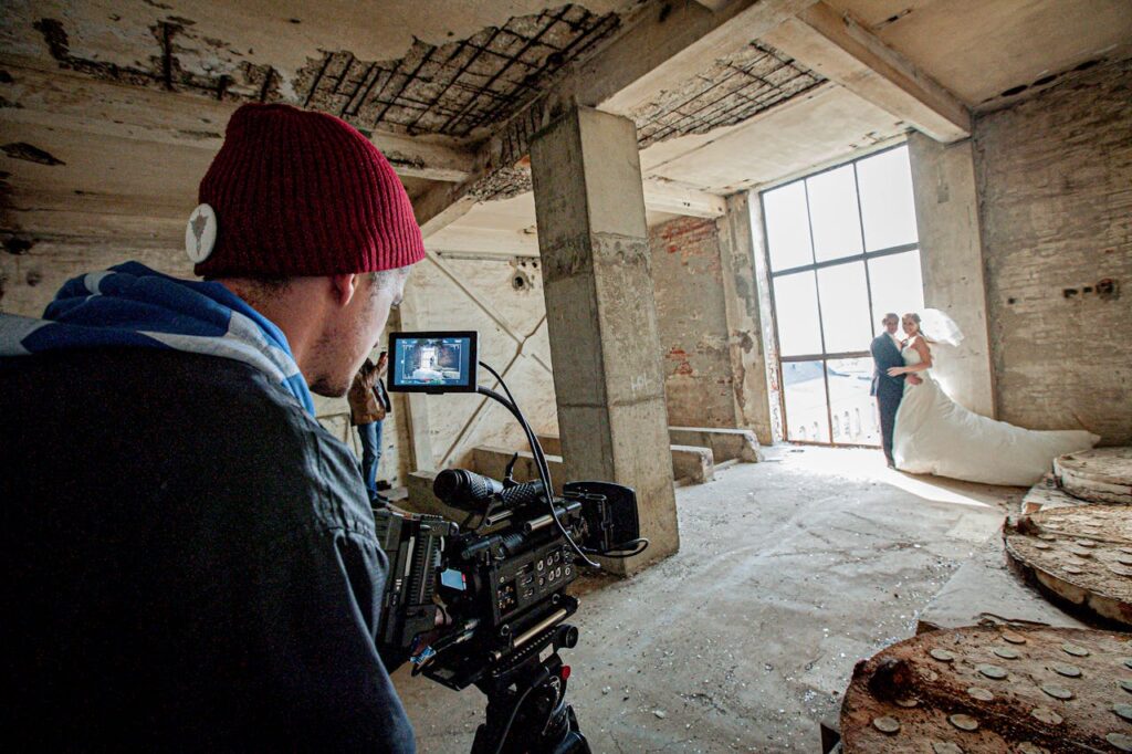 wedding videographer filming bride and groom by large window in ancient building