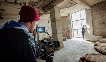 wedding videographer filming bride and groom by large window in ancient building