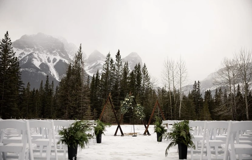 A winter outdoor wedding ceremony in Canmore with white chairs arranged among snow-covered trees, creating a serene and picturesque scene.