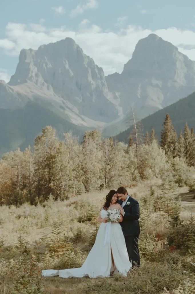 A bride and groom pose together in the picturesque Banff landscape, surrounded by mountains and lush greenery.