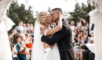 bride and a groom are kissing in front of the wedding guest plus-one