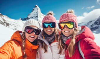 group of bachelorettes pose on snowy mountain in ski suits and goggles winter winter bachelorette getaway