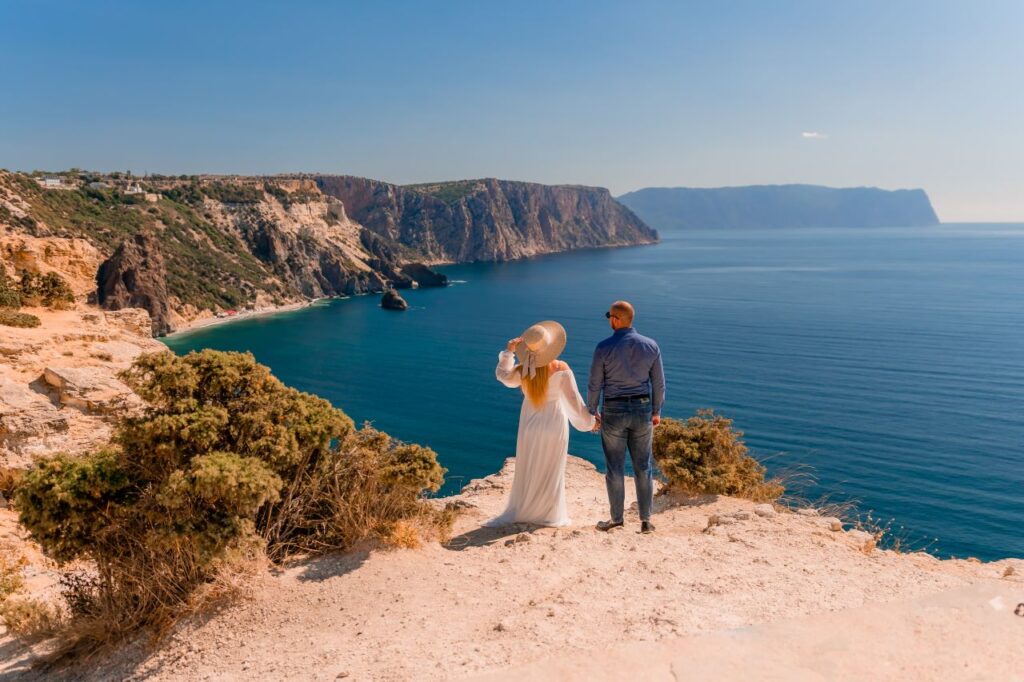 bride and groom pose for photo on cliff while looking at ocean during adventure elopement