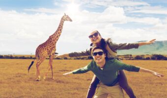 couple pose for portrait on honeymoon safari with giraffe in background