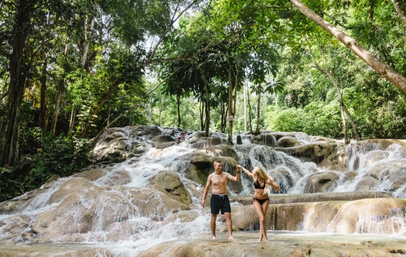 a couple stand before a majestic waterfall, surrounded by lush jungle foliage, in jamaica for their honeymoon