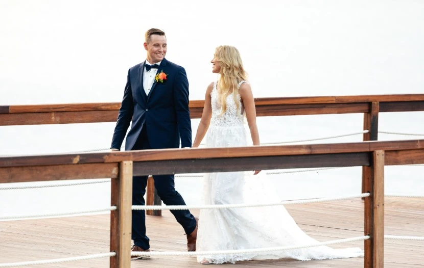 The bride and groom walk together on a picturesque dock, embodying love and joy against a tranquil water backdrop.