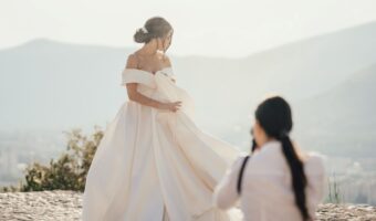 bride poses for portrait with mountain background while wedding content creator snaps photo