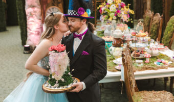 bride and groom kiss while holding cake at Alice in Wonderland-themed wedding