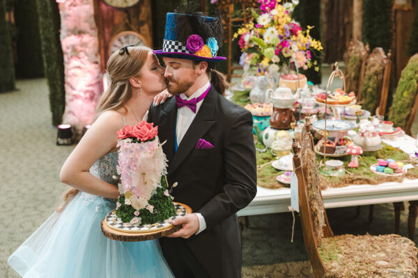 bride and groom kiss while holding cake at Alice in Wonderland-themed wedding
