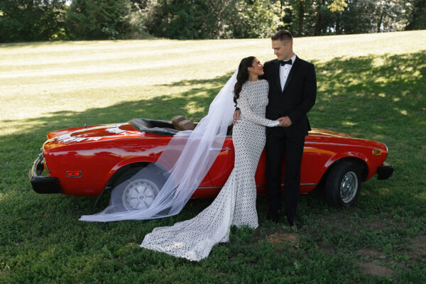 Bride and groom pose next to red convertible sports car at ourdoor wedding at Mt. Lehman Winery