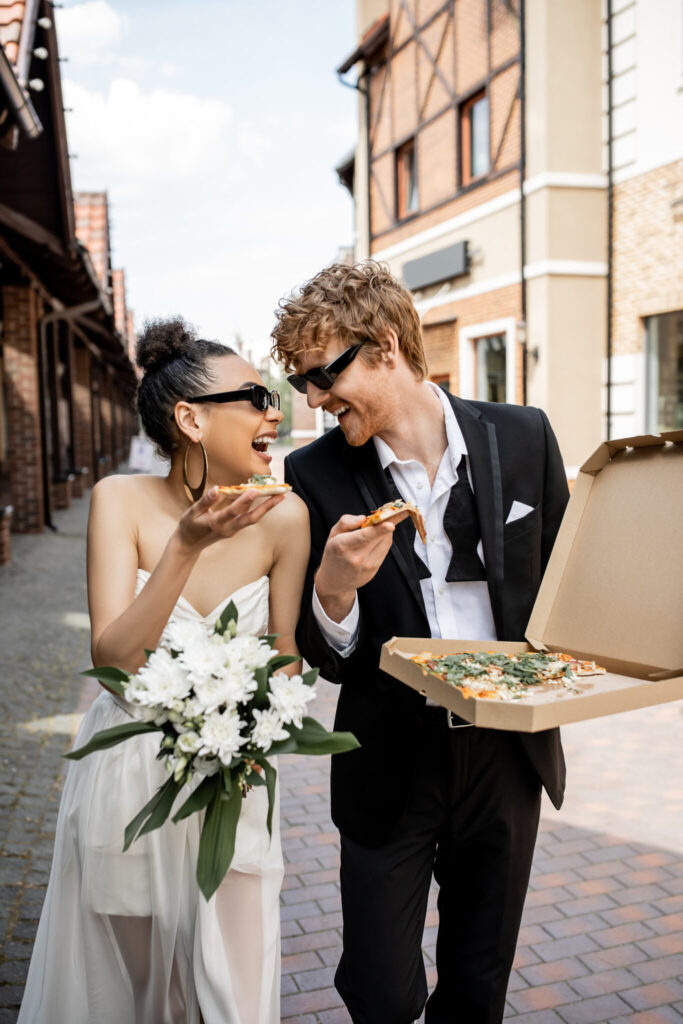 bride and groom in city streets eating pizza after wedding