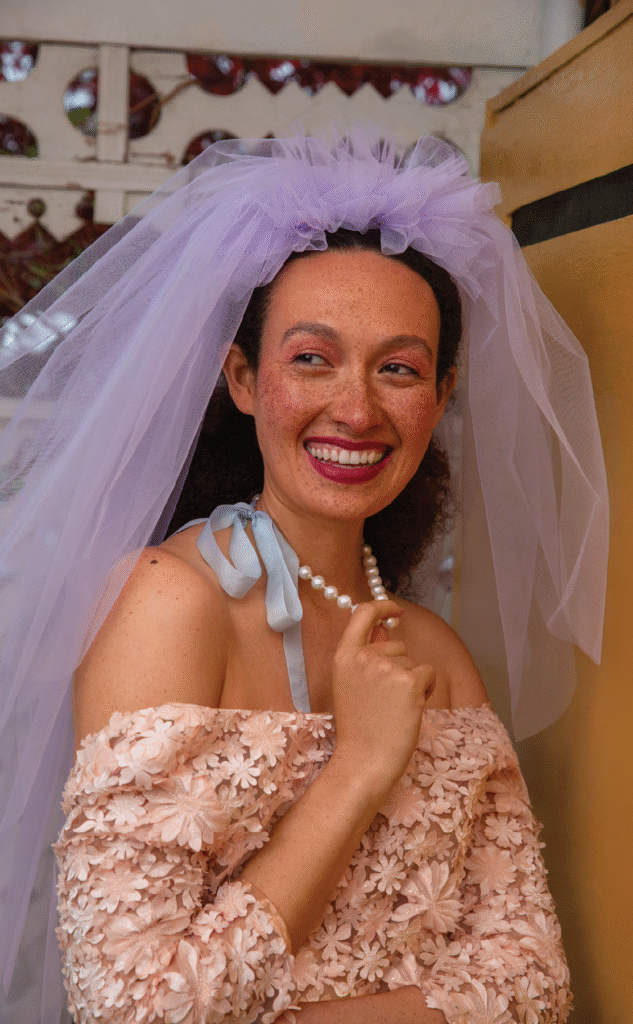 bride smiling at camera while wearing lavender blue veil and blue ribbon around neck blush wedding dress