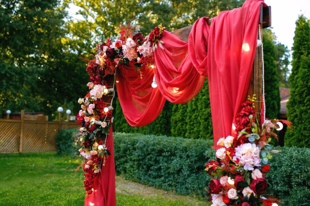 outdoor wedding ceremony with arch that's draped with red drapery and beautiful red and white flowers