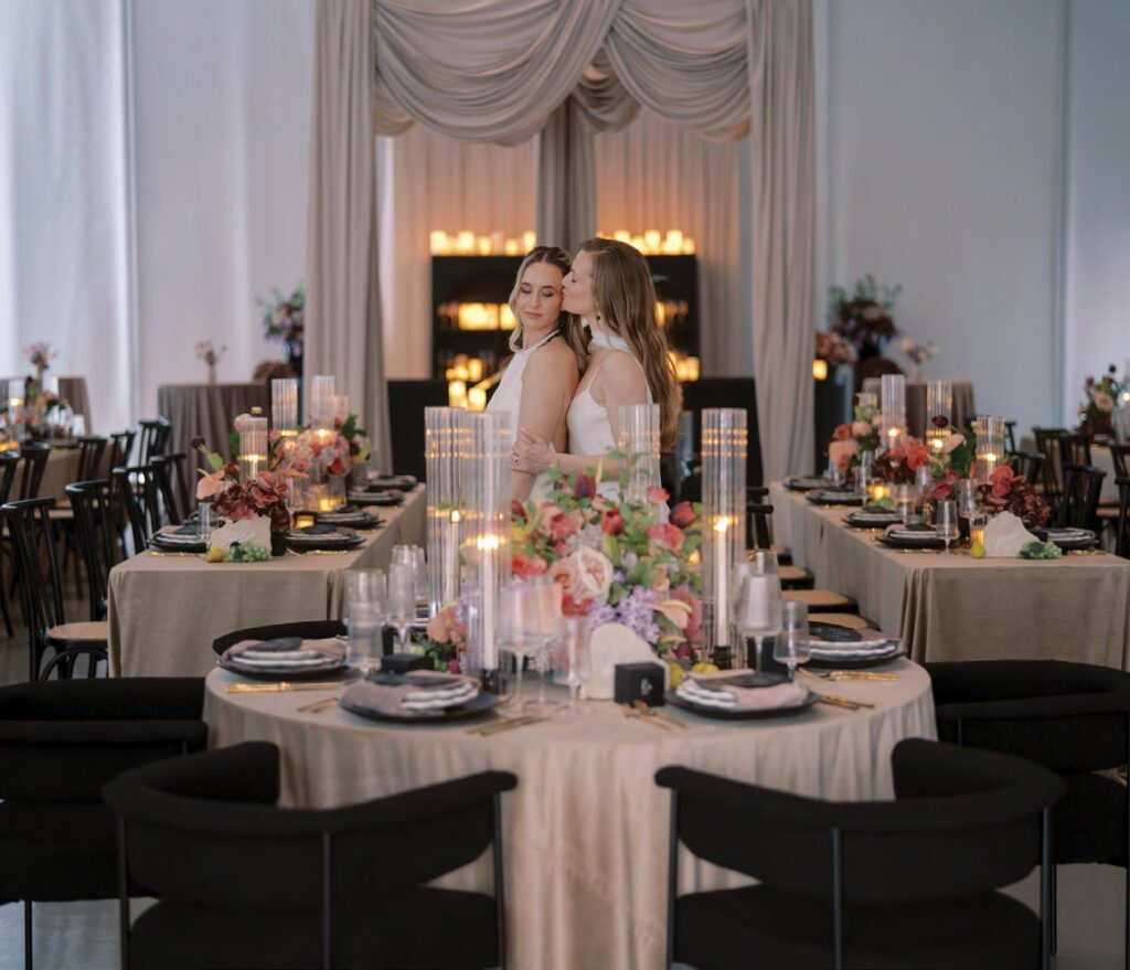 two brides pose for picture next to wedding tables during styled wedding shoot