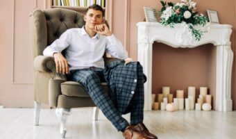 fashion-forward groom trends include checkered and patterned suits worn by groom sittiing in vintage chair