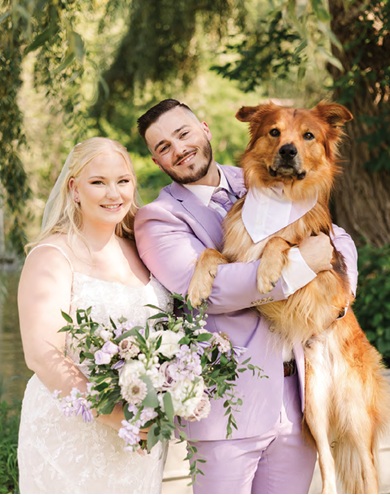 newlyweds holding dog on wedding day outdoor