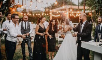 bridal party with man of honour celebrating at outdoor wedding while groom sprays champagne