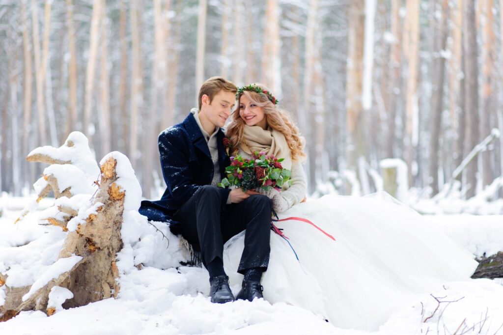winter wedding portrait of bride and groom sitting on log in the snow