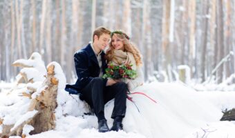 winter wedding portrait of bride and groom sitting on log in the snow