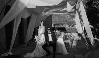 bride in groom pose for black and white portrait wearing sunglasses sitting at reception table under wedding drapery - the hottest 2026 wedding trends