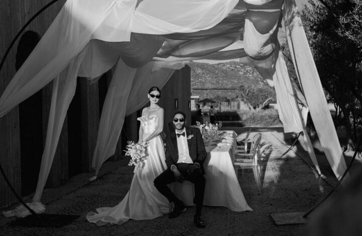 bride in groom pose for black and white portrait wearing sunglasses sitting at reception table under wedding drapery - the hottest 2026 wedding trends