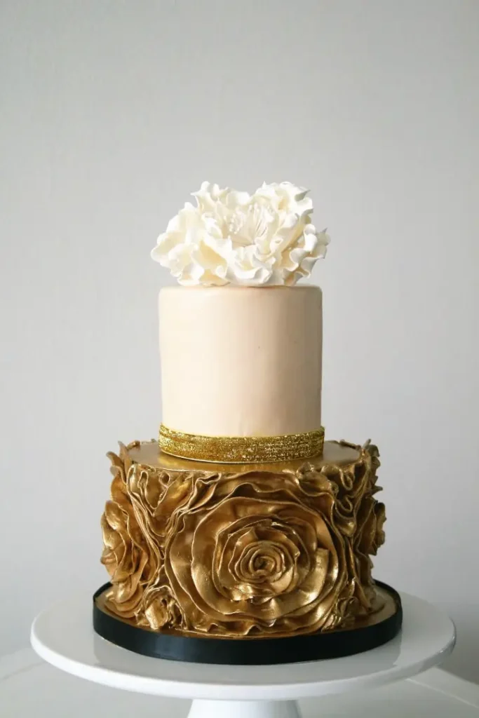 Luxury gold metallic wedding cake with ivory top layer, swirled bottom layer 2026 wedding cake trends
