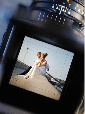 view of honeymoon photographers camera preview image screen of bride and groom sitting on dock at beach