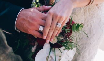 groom and bride hold hands showing men's engagement ring and wedding ring