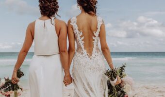 two brides holding hands on the beach at destination wedding