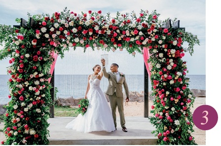 bride and groom pose under tropical wedding arch on beach
