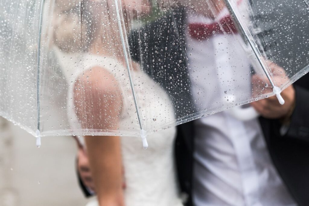 bride and groom in rain with clear umbrella rain on wedding day
