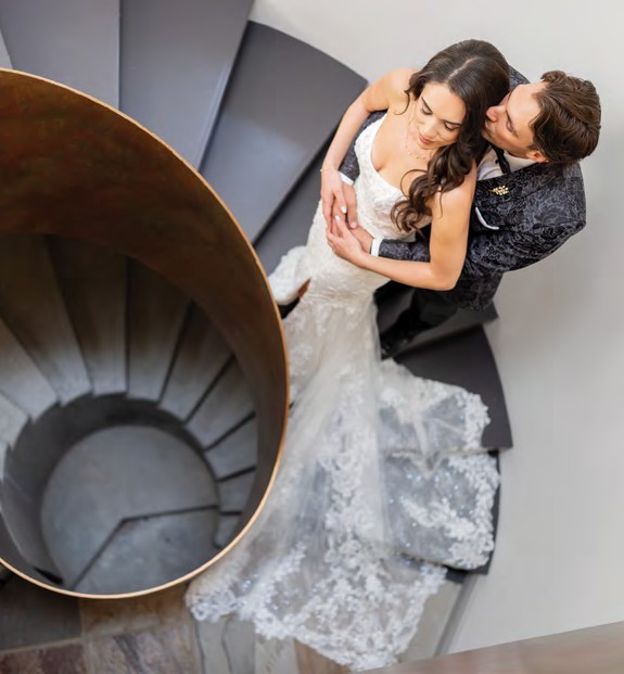 Couple in wedding attire embracing on a spiral staircase, shot from above.