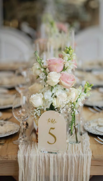 Wedding reception table with pastel floral centerpiece and a 'Table 5' place card on a beige runner.