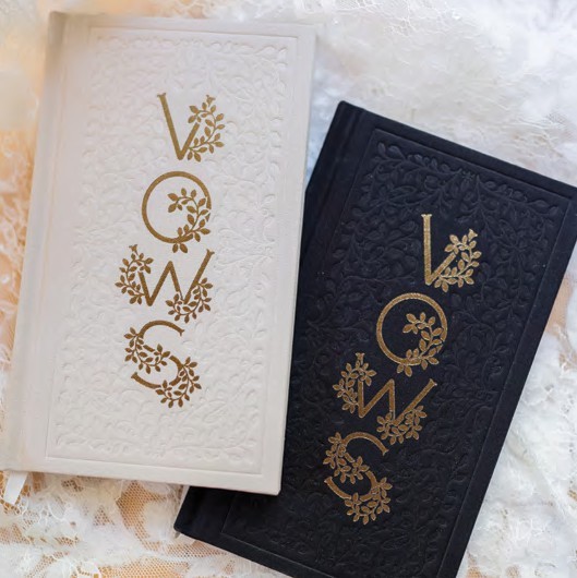 White and black embossed cards with gold floral lettering spelling 'LOVE' arranged vertically, resting on lace fabric.