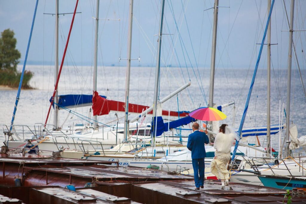 rainy wedding bride and grooom walk on pier next to sailboats after getting destination wedding insurance