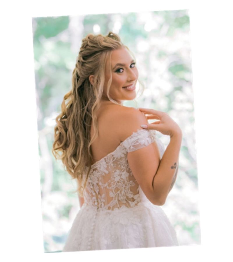 Bride in a lace wedding dress, back view, turning to smile over her shoulder with long wavy hair.