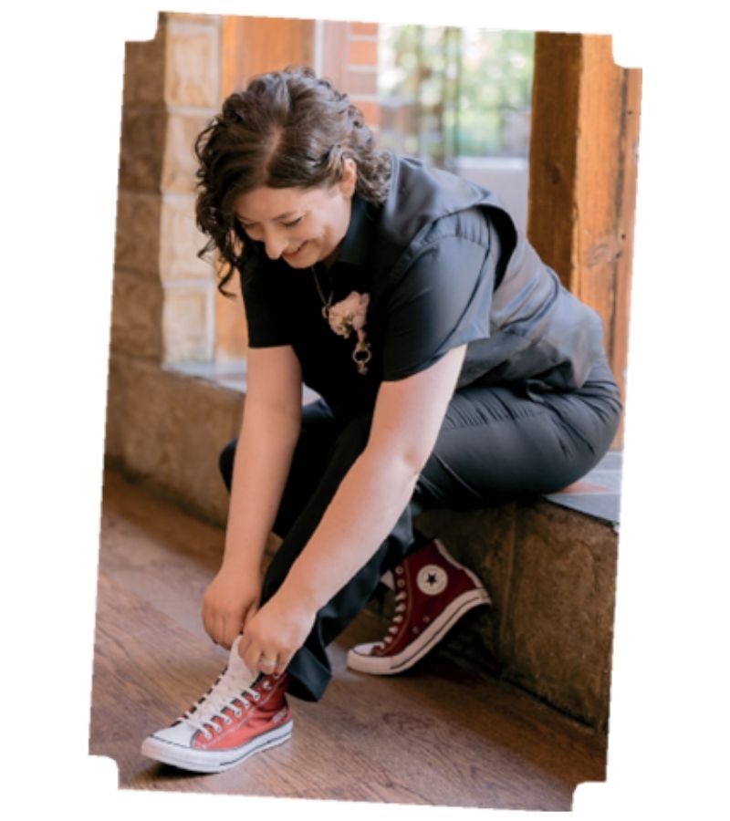 Woman tying the laces of red high-top Converse sneakers while seated on a stone step