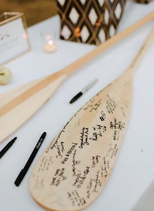 A wooden paddle covered in handwritten messages, lying on a white table with pens and candles nearby at an event.