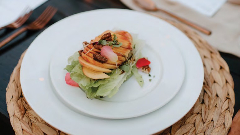 Elegant salad stack: layered apple slices atop mixed greens with nuts and edible petals on a white plate