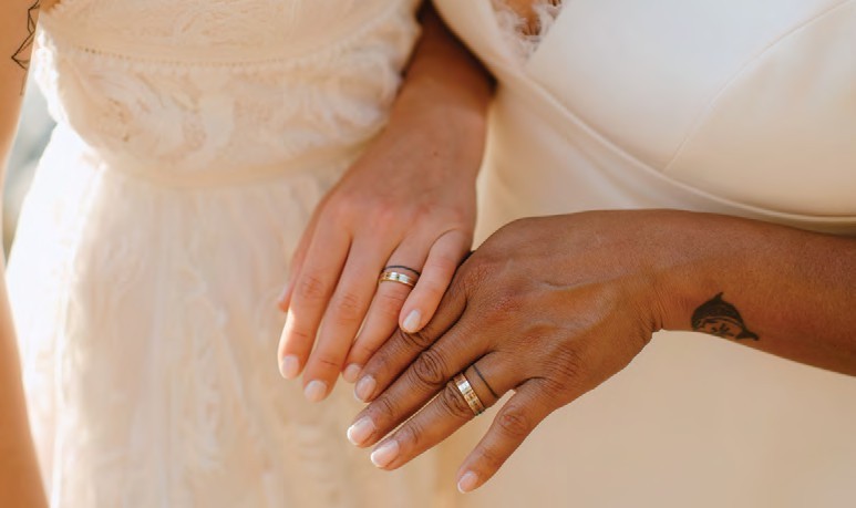 Two hands with wedding rings resting together on a lacy wedding dress close-up, showing interracial couple.