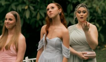 Three women in pastel bridesmaid dresses stand outdoors at an event, looking ahead in calm poses.