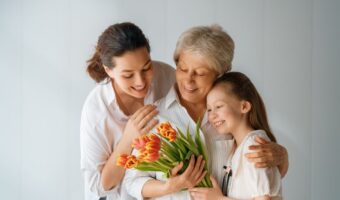 Three generations sharing a hug while holding a bouquet of orange tulips.