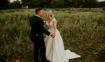 bride and groom laugh while holding hands in a field after talking about wedding planning mistakes