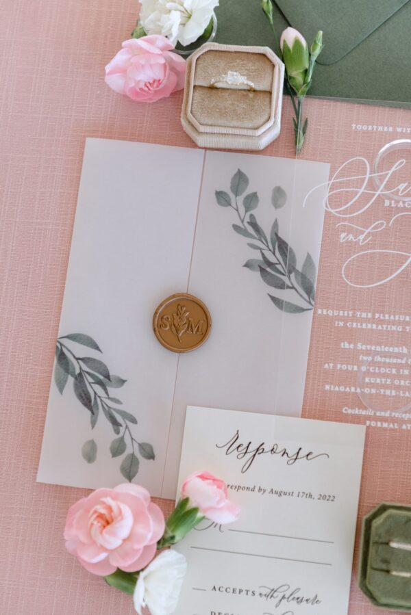Wedding invitation suite with pink flowers, a gold ring in a velvet box, and botanical illustrations on a pink backdrop, conveying a wedding theme.