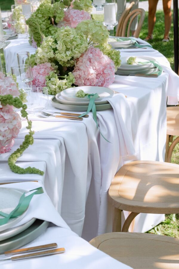 Outdoor dining table decorated with pink and green hydrangea centerpieces, white linens, and mint ribbons.