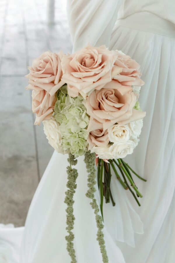 Bride holds a pastel pink rose bouquet with white hydrangeas against a white dress backdrop.