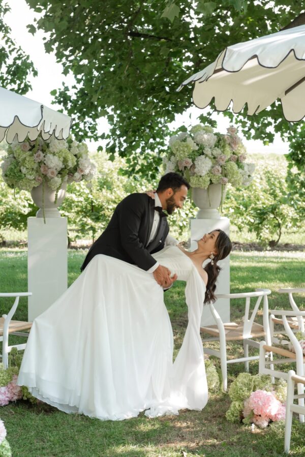 Bride and groom dance outdoors under white canopies with lush floral arrangements surrounding them.