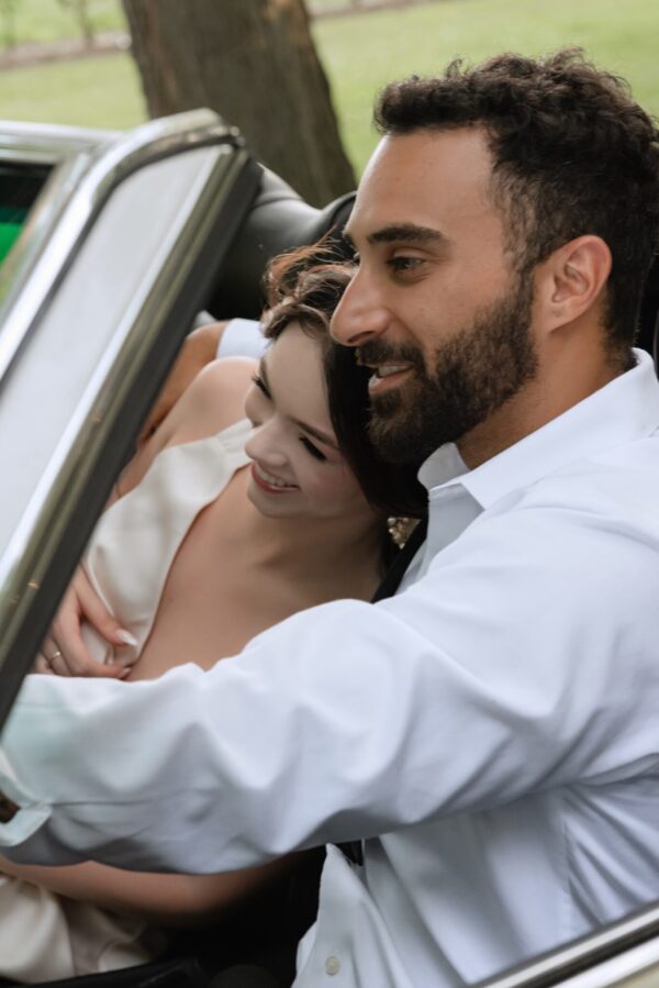 Couple leaning together in a car, the woman resting against the man as they smile inside an open vehicle window